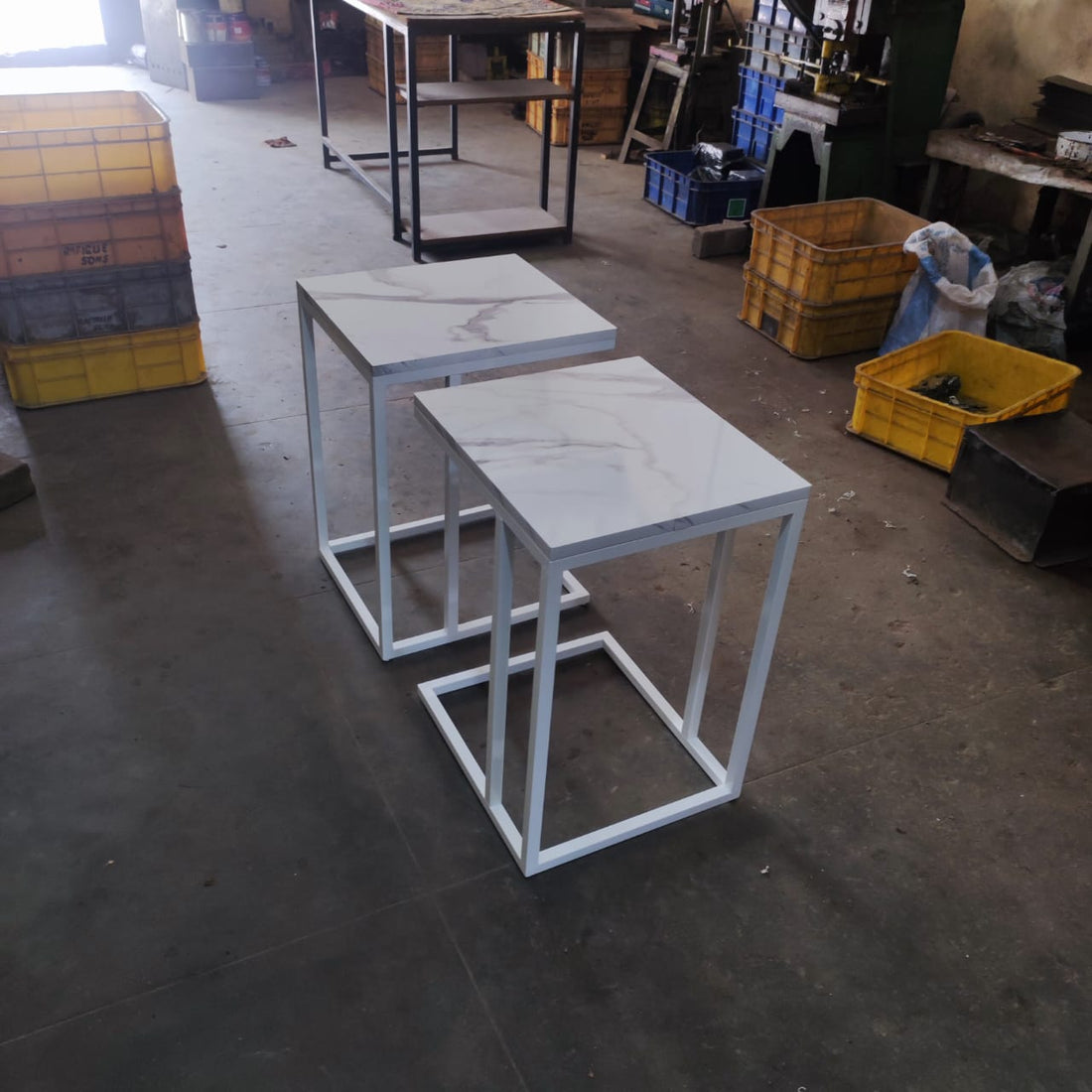Two marble-finish laptop tables standing in a factory after production, showcasing their sleek design and sturdy metal frames.
