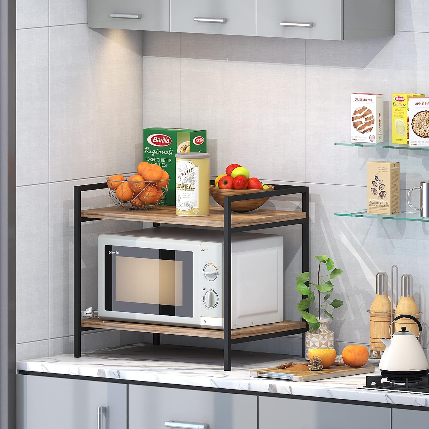 A black microwave stand with a wooden top, placed on a kitchen counter next to a microwave oven, with various kitchen items like oranges and apples on the stand.